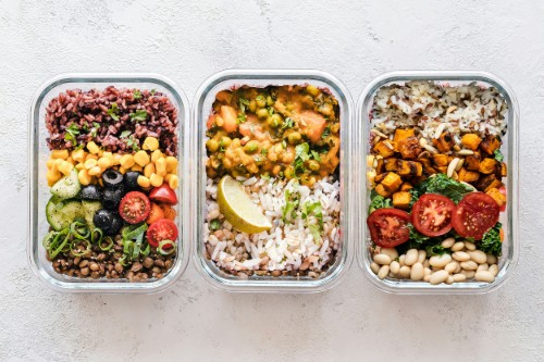 three separate healthy lunches in rectangular containers sit on a white table
